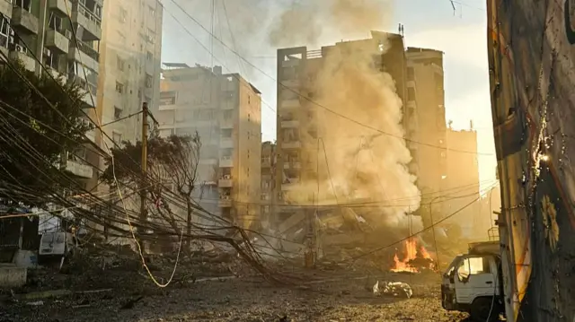 Yıkılmış binalar arasından güneş doğarken dumanlar yükseliyor