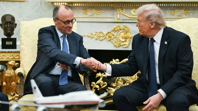 Merz le estrecha la mano a Trump, ambos sentados en el Salón Oval de la Casa Blanca