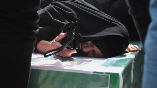 Uma mulher chorando em cima de um caixão