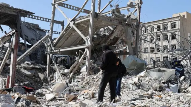 Yıkılmış bir binanın enkazında ayakta duran iki kişi