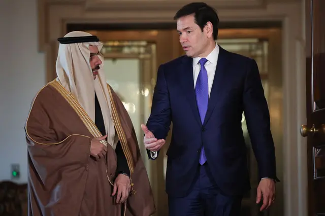 روبيو يرتدي بدلة رسمية كحلية اللون يتحدث إلى الأمير السعودي الذي يلبس العباءة والثوب السعودي التقليدي باللونين البني والأسود.