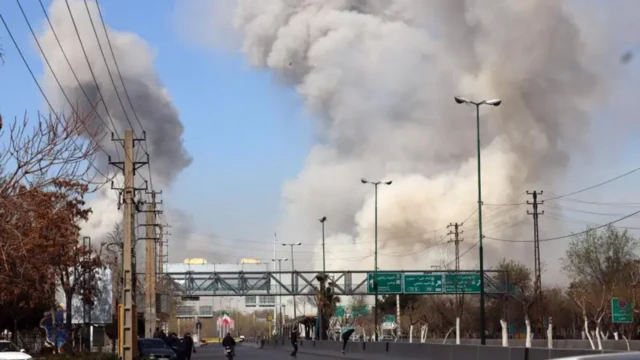 Colunas de fumaça são vistas ao fundo de uma estrada em Teerã
