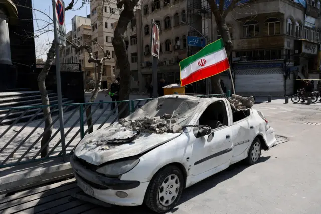 Tahran'da tahrip olmuş bir otomobilde İran bayrağı asılı.