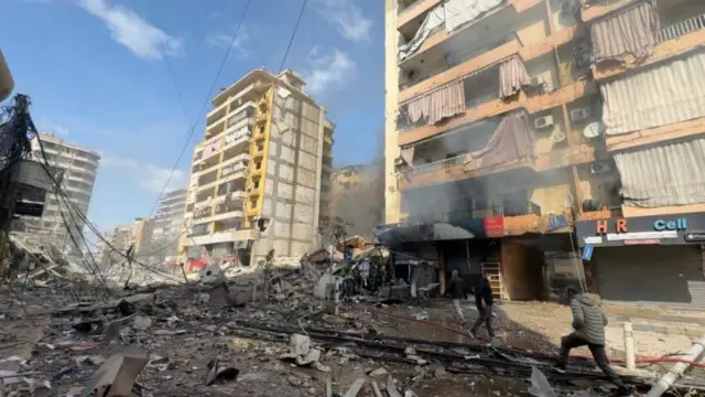 مردم در بیروت، لبنان، در تاریخ ۴ مارس، از میان آوار و خرابه‌های جلوی ساختمان‌های آسیب‌دیده در جریان حملات هوایی عبور می‌کنند