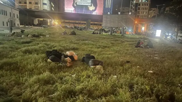 حديقة في بيروت وبها متعلقات أشخاص، مليئة بالعشب الأخضر. الصورة التقطت ليلاً.