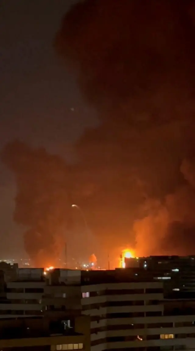 لهيب أحمر يشتعل في السماء فوق بعض ناطحات السحاب ليلًا.