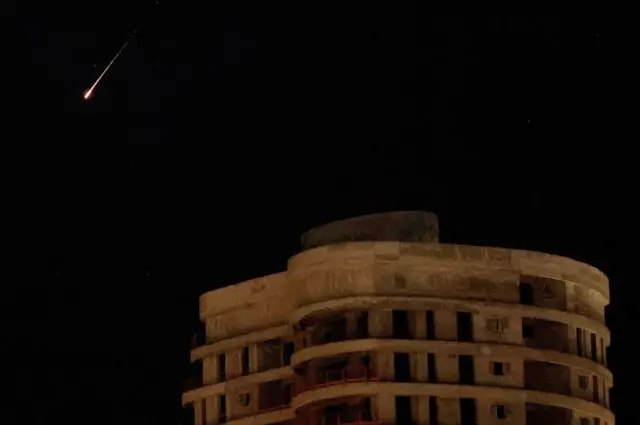 O rastro de um míssil ilumina o céu noturno acima de Netanya, cidade costeira e ponto turístico de Israel, acionando as sirenes de alerta aéreo.