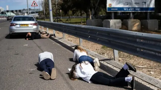 Pessoas deitadas em uma estrada com as mãos na cabeça