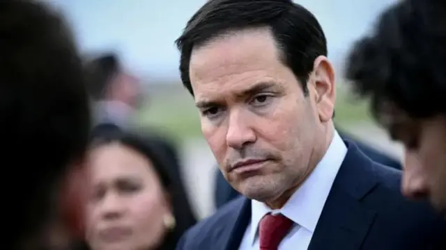 Minisitiri w'ububanyi n'amahanga w'Amerika Marco Rubio arimo kureba muri 'camera' akikijwe n'abandi bantu. Yambaye ikositimu na karuvati.