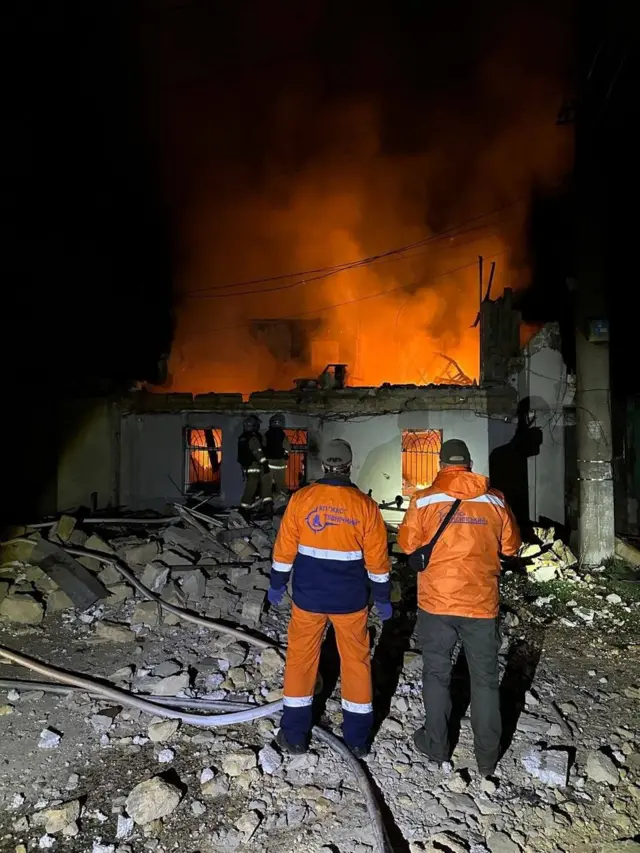 Спасатели на фоне горящего дома