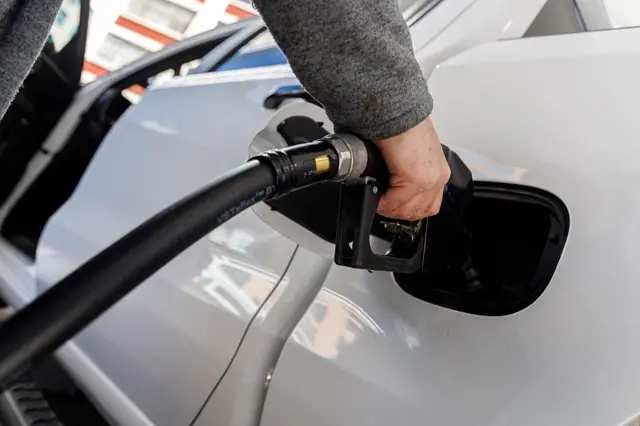 يد شخص تضع خرطوم توصيل البنزين لنقل الوقود من الخزان إلى محرك سيارة.