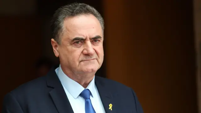 اسرائيل کاتز با کت و کراوات سرمه‌ای و روبان زرد بر یقه