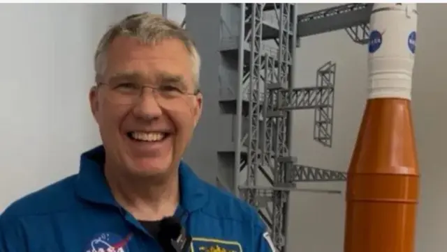 Stephen Bowen yifubitse ikote ry’ibara risa n’ubururu, yafotowe yishimye aseka.