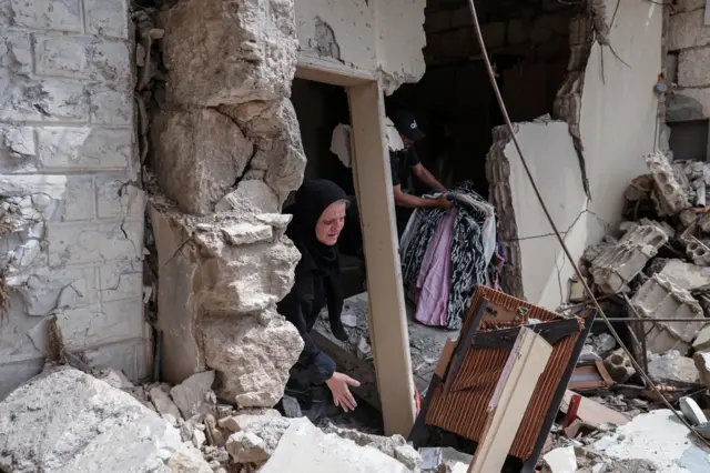 زهرة عيد، 60 عامًا، نازحة من قضاء جبيل، تنقذ بعضًا من ممتلكاتها من منزلها الذي دمرته الغارات الإسرائيلية، بعد عودتها إلى قريتها عقب وقف إطلاق النار بين لبنان وإسرائيل، في طير دبا، جنوب لبنان، 18 أبريل/نيسان 2026