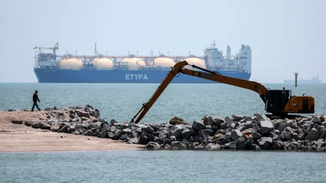 ကမ်းခြေက ဝန်မစက်တစ်ခုနားမှာ လူတစ်ဦး ကျောက်တုံးတွေနား လမ်းလျှောက်နေပြီး အနောက်ဘက်က ရေပြင်ကျယ်မှာတော့ "ETYFA" စာလုံးတပ်ထားတဲ့ သင်္ဘောတစ်စင်းကို မြင်ရ