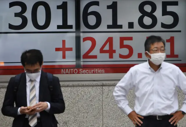 رجلان يقفان أمام شاشة إلكترونية تعرض متوسط المؤشر نيكي الياباني