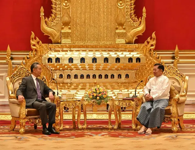 တရုတ်နိုင်ငံခြားရေးဝန်ကြီးရဲ့ ၂၀၂၄ ခုနှစ်၊ သြဂုတ်လလယ်ပိုင်း နေပြည်တော်ခရီးစဉ်မှာ မြန်မာစစ်ခေါင်းဆောင် ဗိုလ်ချုပ်မှူးကြီး မင်းအောင်လှိုင်နဲ့ တွေ့ဆုံမှုလို့ နှစ်နိုင်ငံသတင်းထုတ်ပြန်တဲ့ဓာတ်ပုံဖြစ်ပါတယ်။ဓာတ်ပုံဝဲဘက်မှာ တရုတ်နိုင်ငံခြားရေးဝန်ကြီး ဝမ်ယိက အနောက်တိုင်းဝတ်စုံနဲ့ ညာဘက်လှည့်စကားပြောနေပြီး ဓာတ်ပုံ ဘယ်ဘက်မှာ ဦးမင်းအောင်လှိုင်က တိုက်ပုံအဖြူဝတ် ပုဆိုးဝတ်ထားပြီး ဝမ်ယိဘက်ကို လှည့်စကားပြောနေ။ သူတို့ နှစ်ဦးအနောက်မှာ သံတမန်ဆောင် ဧည့်ခန်းမ အပြင်အဆင်ရှိနေ