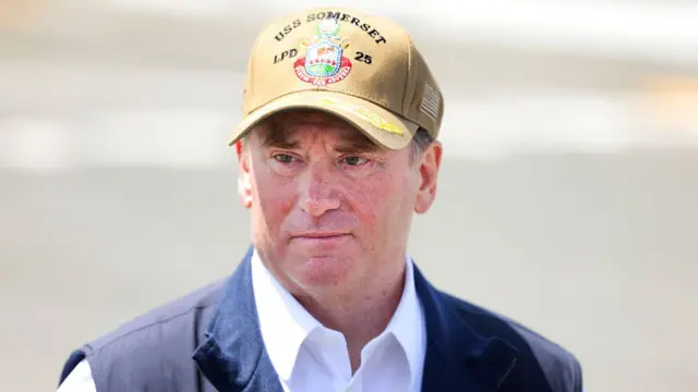 جان فِلان، وزیر نیروی دریایی آمریکا با کلاه ارتشی و جلیقه آبی