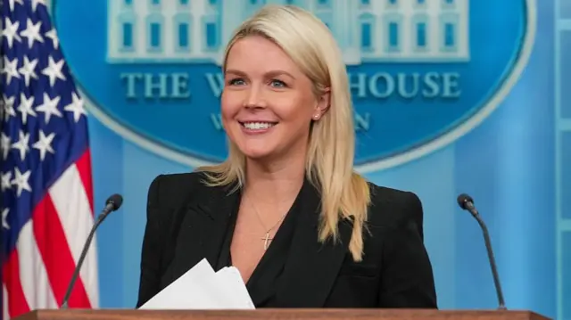 کارولین لویت با کت سیاه پشت تریبون کاخ سفید