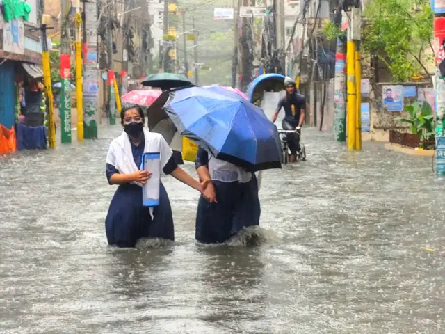 দু'টি কিশোরি হাত ধরে হাঁটু সমান বৃষ্টির পানির মধ্য দিয়ে হাঁটছে