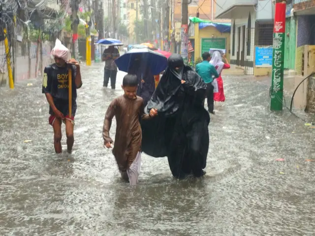 একজন কালো বোরখা পরা নারী ও একটি শিশু বৃষ্টির পানিতে হেঁটে যাচ্ছে