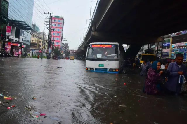 বৃষ্টির পানির মাঝেই প্রায় ডুবে আছে বাস, মানুষ হেঁটে যাচ্ছে