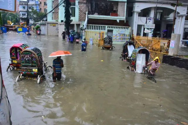 সড়কে পানি উঠে গেছে। তার মাঝ দিয়ে হেঁটে যাচ্ছে মানুষ, চলছে রিকশা