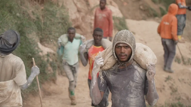 Abakozi barimo gukora mu kirombe cya Rubaya mu ntara ya Kivu ya Ruguru, mu burasirazuba bwa DRC. Batatu bikoreye imifuka ku bitugu.