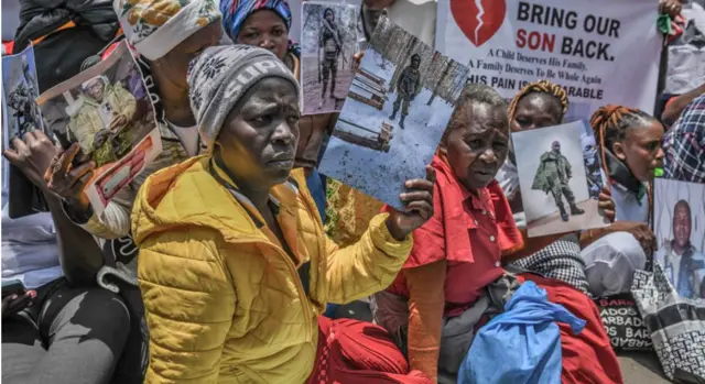 Itsinda ry’abagore b’Abanya-Kenya—umwe yambaye ikote rinini ry’umuhondo, undi yambaye ikanzu itukura—bicaye mu muhanda mu myigaragambyo yabereye mu mujyi wa Nairobi, bafashe amafoto ya benewabo bambaye imyenda ya gisirikare igaragaza ko bari mu gisirikare cy’Uburusiya mu ntambara yo muri Ukraine. Hari n’ufashe icyapa cyanditseho ngo “Mudufashe dusubizwe umwana wacu.”