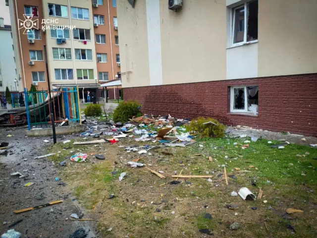 Поврежденный подвальный и первый этаж дома, обломки на земле около детской площадки.