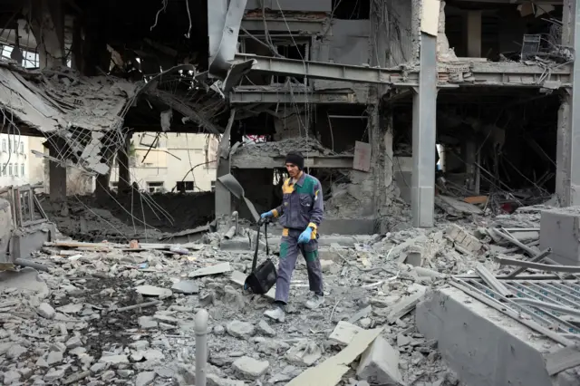 তেহরানে হামলায় ক্ষতিগ্রস্ত একটি ভবনের সামনে এক ব্যক্তি একটি ব্যাগ নিয়ে হেঁটে যাচ্ছেন