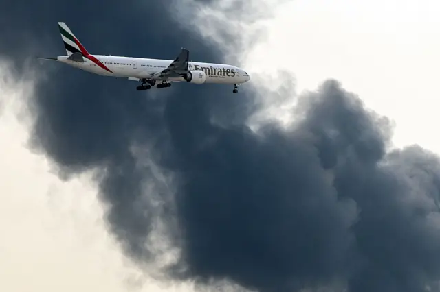 طائرة بوينغ 777 تابعة لشركة طيران الإمارات تستعد للهبوط بينما يتصاعد عمود من الدخان من حريق مستمر بالقرب من مطار دبي الدولي في دبي في 16 مارس/آذار 2026.
