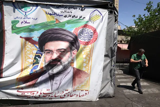 رجل يمر بجوار لافتة منصوبة على جانب الطريق تحمل صورة المرشد الأعلى الإيراني آية الله مجتبى خامنئي، في طهران في 29 أبريل/نيسان عام 2026.