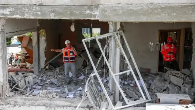 مبنى متضرر في مدينة رمات غان في إسرائيل يقف قربه عاملا إنقاذ.