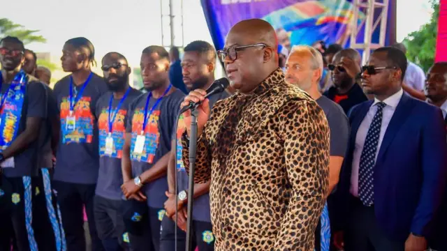 Perezid Félix Tshisekedi ahagaze arimo kuvugira mu ndangururamajwi, akikijwe n'abakinnyi b'ikipe y'igihugu n'umutoza wabo.