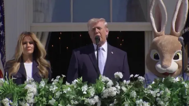 دونالد ترامب يتحدث في الميكروفون. إلى يساره ميلانيا ترامب، وإلى يمينه شخص يرتدي زي الأرنب التنكري بمناسبة عيد الفصح.