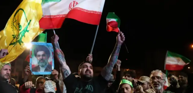 Abanya-Iran bari mu byishimo nyuma y’agahenge katangajwe, umwe afite ifoto iriho umugabo ufite ubwanwa burimo imvi uteze igitambaro mu mutwe.