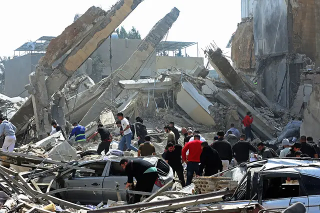 أشخاص يتجمعون حول ركام مبنى وسيارات مدمرة من غارة جوية