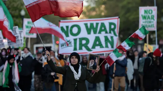 محتجون في واشنطن ينددون بالعمل العسكري الأمريكي ضد إيران ويرفعون العلم الإيراني وعدداً من اللافتات.