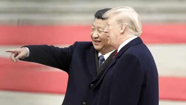 Perezida Xi na Perezida Trump bambaye amakoti maremare y'umukara, Perezida Xi amutungiye urutoki ahantu hatagaragara ku ifoto, amwenyura.