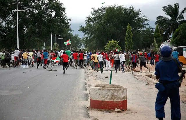 Abantu benshi barimo kwiruka mu muhanda wa kaburimbo, mu myigaragamyo i Bujumbura, mu Burundi, ku itariki ya 13 Gicurasi (5) mu 2015, umupolisi ufite imbunda ahaze ku ruhande rw'umuhanda abareba, yambaye 'casque' y'ubururu n'imyenda y'akazi y'ubururu.