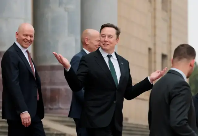Ifoto ya Elon Musk ariko yerekana ibiganza amwenyura.