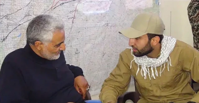 محمد باقر يرتدي ملابس صفراء وقبعة رياضية على رأسه بنفس اللون مع وشاح، ويجلس بجوار قاسم سليماني، قائد فيلق القدس الراحل في صورة غير محددة التاريخ.