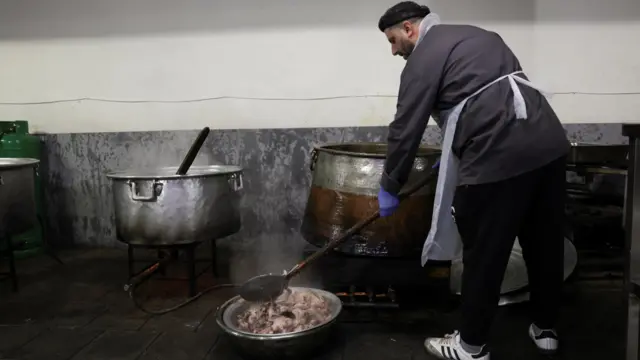 رجل يطبخ في أوانٍ كبيرة لمجموعة نازحين في مدرسة تحولت لمركز إيواء.