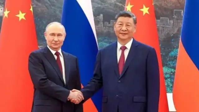 Perezida Putin na Perezida Xi bahanye ikiganza, inyuma yabo hari amabendera y'ibihugu byombi.
