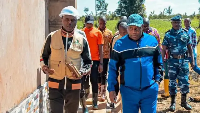 Prezida Evariste Ndayishimiye atambuka ari kumwe na Léonidas Nibigira, inyuma yabo hari abantu benshi harimwo n'umusirikare