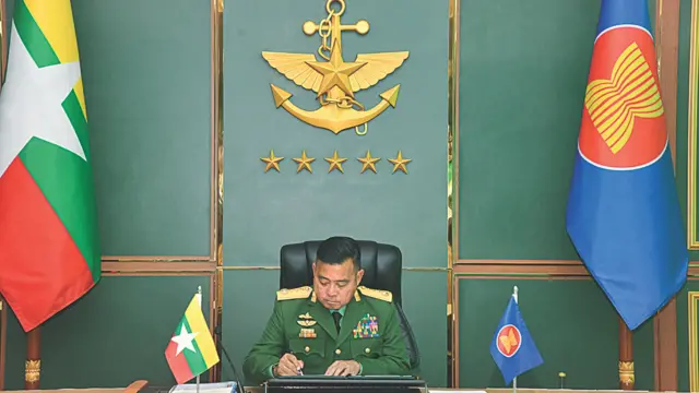 အာဆီယံတပ်မတော်ကာကွယ်ရေးဦးစီးချုပ်များအစည်းအဝေးတက်နေတဲ့ ဗိုလ်ချုပ်ကြီး ရဲဝင်းဦး။ တဖက်တချက်စီမှာ မြန်မာအလံနဲ့ အာဆီယံအလံကိုတွေ့ရပြီး နောက်ခံနံရံမှာ တပ်မတော်အမှတ်တံဆိပ်ရှိနေပါတယ်။