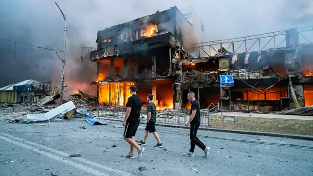 Горящее здание и люди на его фоне в Киеве после российской атаки