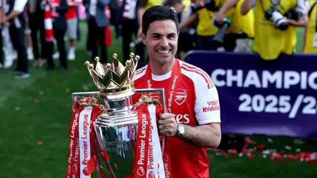 Umutoza wa Arsenal Mikel Arteta ateruye igikombe cya Premier League. Yambaye umupira w'umutuku n'umweru.