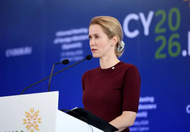 Кая Каллас на белой трибуне на синем фоне